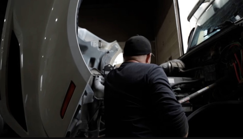 Mechanic leaning into a semi truck engine bay performing maintenance